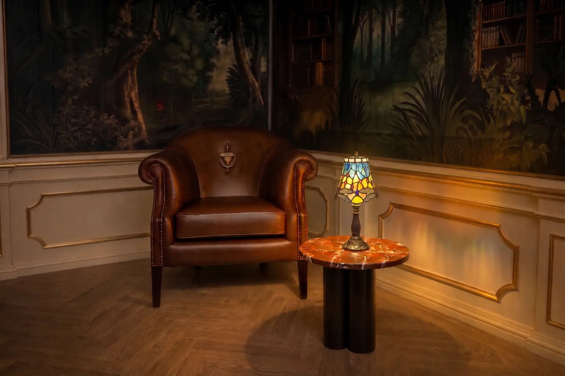 Brandende Tiffany tafellamp 7003 met libellenmotief op een houten bijzettafel in een klassieke leeshoek met fauteuil en boekenkast | RORUVERA