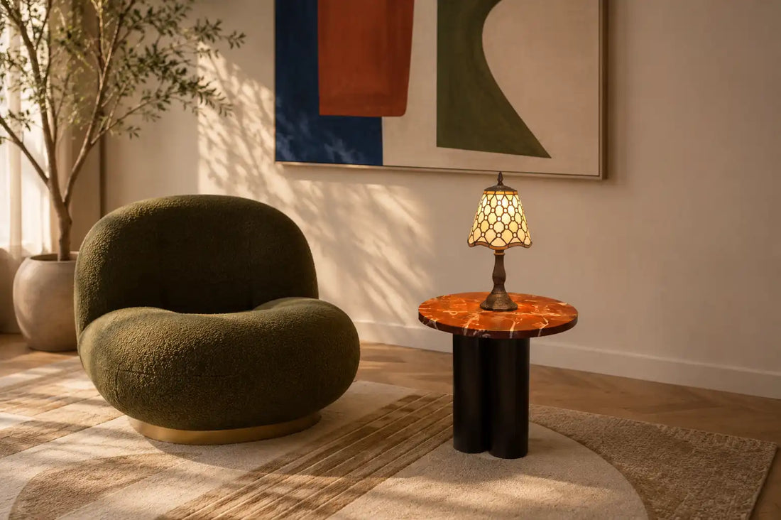 Brandende Tiffany tafellamp 7004 op een marmeren bijzettafel naast een groene designfauteuil in een hip, eigentijds interieur | RORUVERA