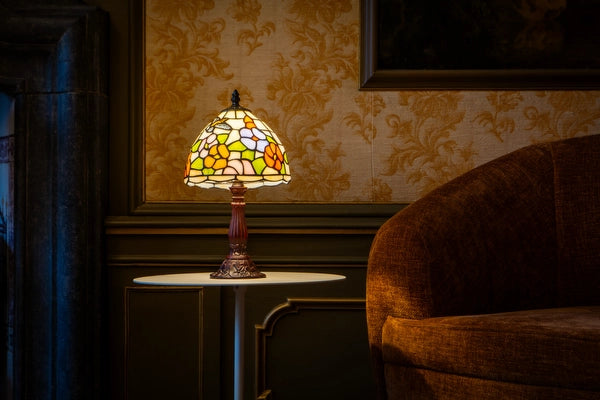 7005 - Tiffany tafellamp met kolibrie- en bloemmotief op een ronde witte bijzettafel naast een fauteuil | RORUVERA