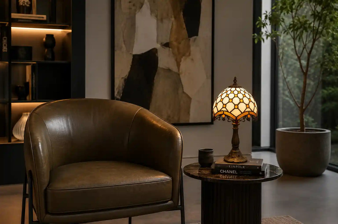 Tiffany tafellamp met crème glas-in-lood kap op een donker bijzettafeltje naast een leren fauteuil in een moderne woonkamer | RORUVERA