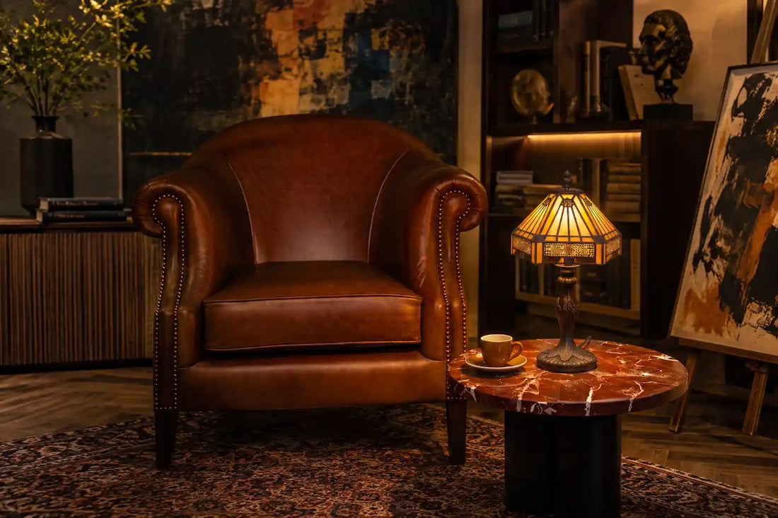 Tiffany tafellamp met geometrisch amberkleurig glas op marmeren tafel in artistiek interieur met leren fauteuil, kunst en boekenkast | RORUVERA