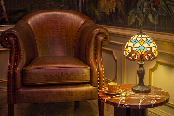 Tiffany tafellamp met kleurrijk glas-in-lood op marmeren bijzettafel naast bruine leren fauteuil in klassiek interieur | RORUVERA