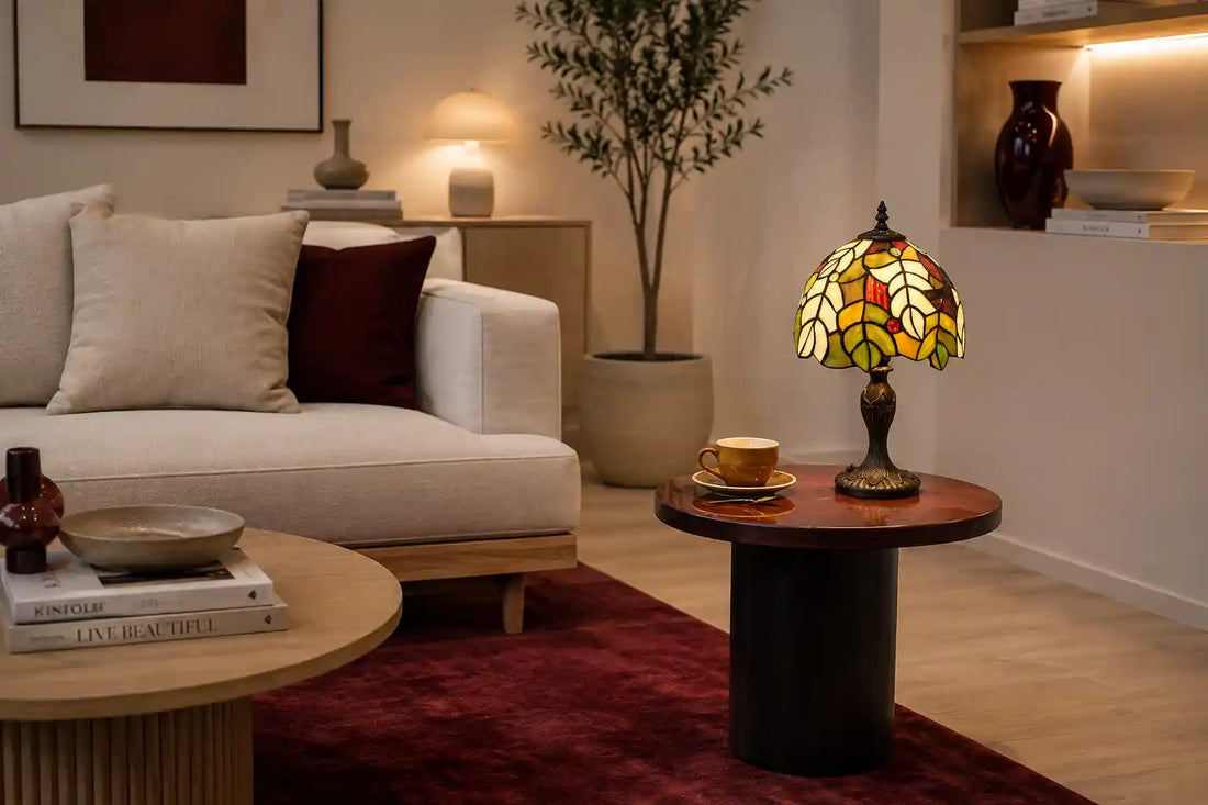 Tiffany tafellamp met groen en crème bladmotief op donkere bijzettafel in moderne woonkamer met lichte bank en bordeauxrood vloerkleed | RORUVERA