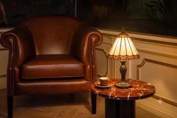Tiffany tafellamp met crème zuilpanelen en amberkleurige details op marmeren bijzettafel naast bruine leren fauteuil | RORUVERA