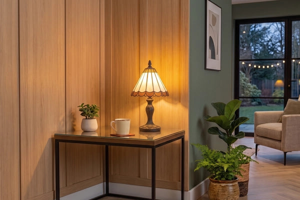 Tiffany tafellamp met crème zuilpanelen en amberkleurige rand op glazen sidetable tegen houten wand in een moderne woonkamer met planten | RORUVERA