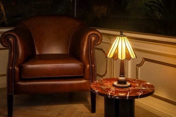 7019 - Tiffany tafellamp met crèmekleurige glazen kap op een marmeren bijzettafel naast een leren fauteuil | RORUVERA