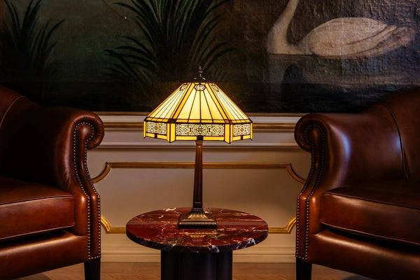 7023 - Tiffany tafellamp met geometrische glazen kap op een marmeren bijzettafel tussen twee leren fauteuils | RORUVERA
