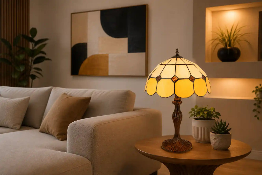 Tiffany tafellamp met geometrische kap in crème en warme ambergele tinten op een ronde houten bijzettafel in een moderne woonkamer met lichte bank, abstracte kunst en kleine groene planten | RORUVERA