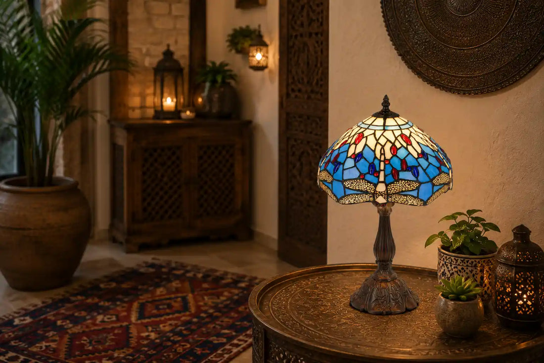 Tiffany tafellamp met blauw-crème libellenmotief en rode glasaccenten op een sierlijke metalen tafel in een warme wereldse woonomgeving met hout, planten, lantaarns en een kleurrijk geweven vloerkleed | RORUVERA