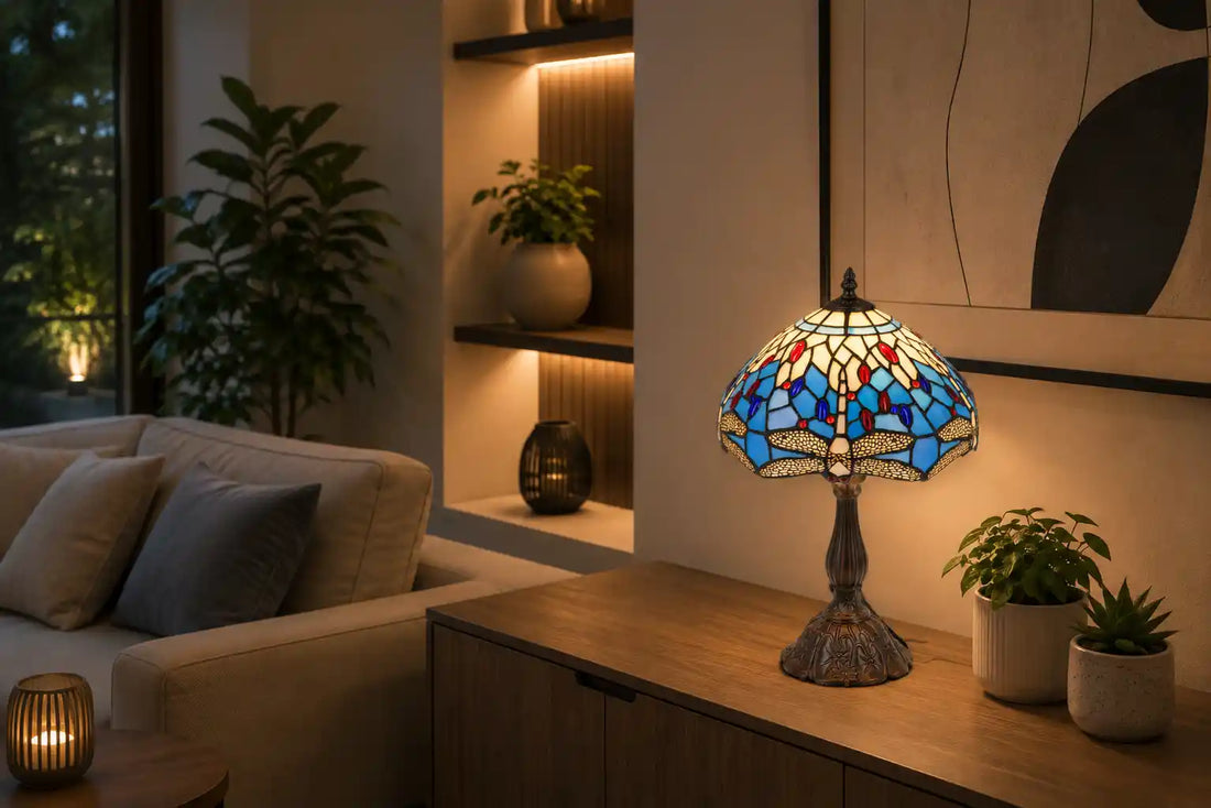 Tiffany tafellamp met libellenmotief in blauw, crème en rode glasaccenten op een houten dressoir in een moderne woonkamer met neutrale meubels, abstracte kunst en groene planten  | RORUVERA
