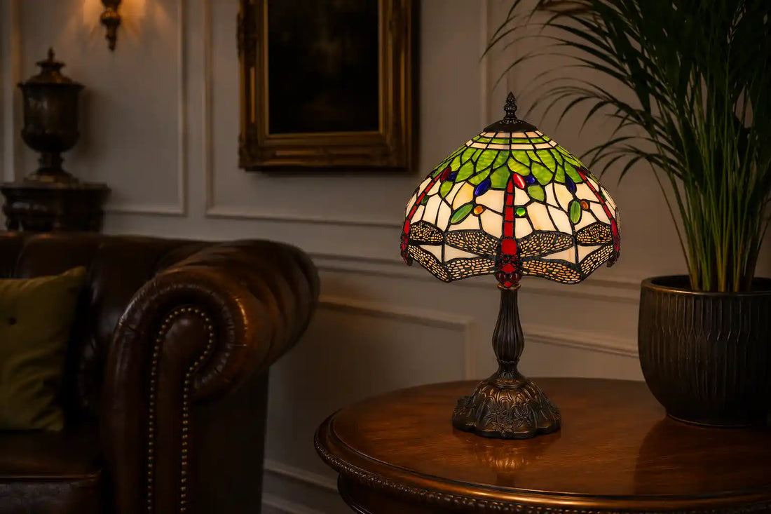 Tiffany tafellamp met libellenmotief in groen, rood en crèmekleurig glas-in-lood, sfeervol geplaatst op een bijzettafel in een klassiek-moderne woonkamer met een grote groene plant | RORUVERA