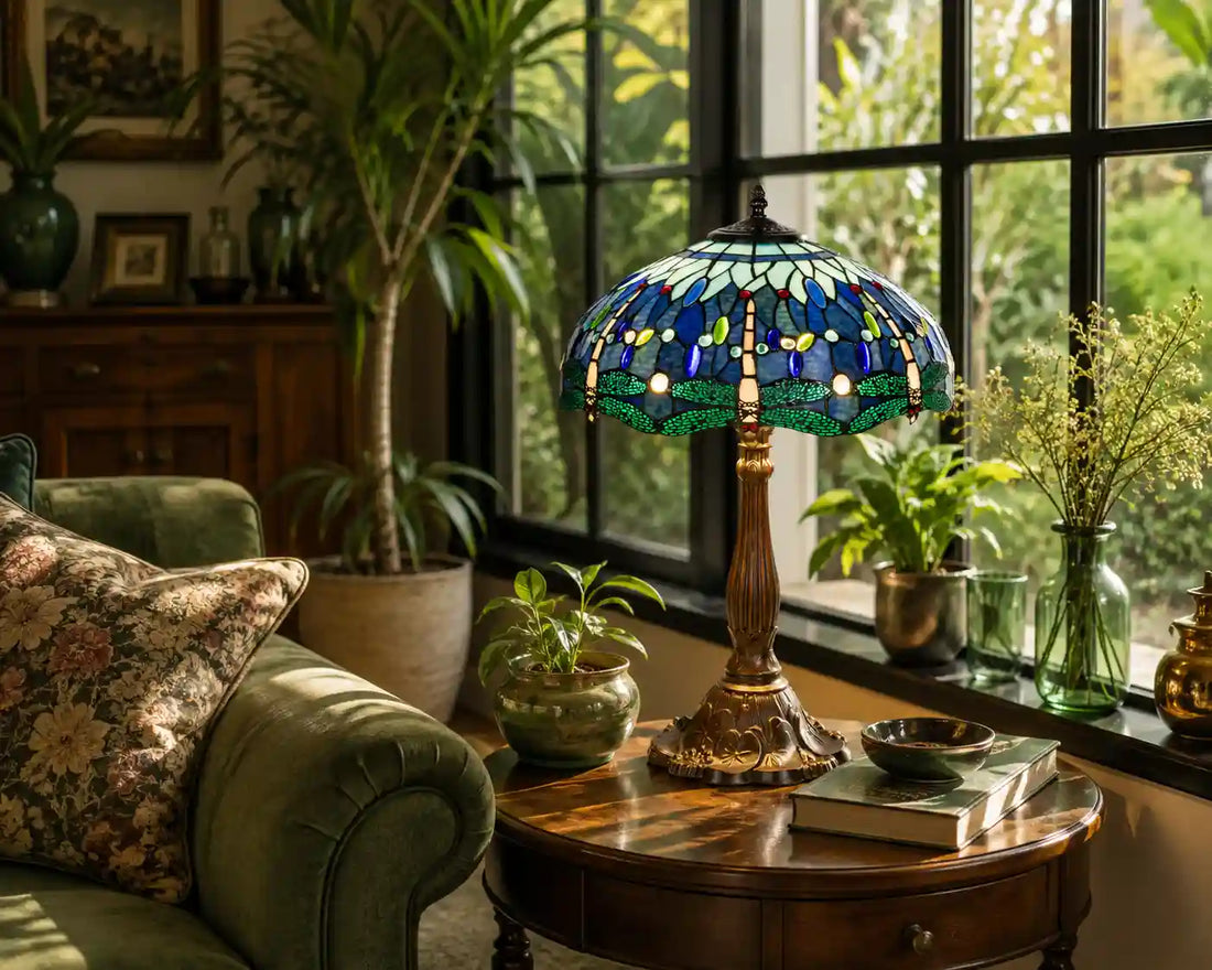 Tiffany tafellamp met libellen in blauw, groen en turquoise glas-in-lood, sfeervol geplaatst bij een groene fauteuil en planten voor een groot raam | RORUVERA
