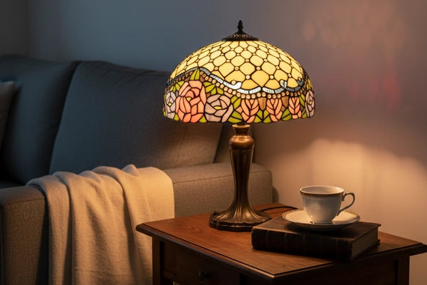 Tiffany tafellamp met rozenmotief in roze, crème en groen naast donkere bank op houten bijzettafel in sfeervol interieur  RORUVERA