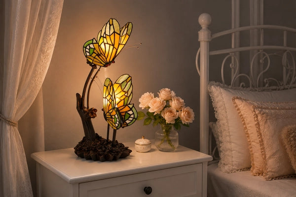 Tiffany dubbele vlinderlamp 7055 in amber, groen en crème op een wit nachtkastje naast het bed | RORUVERA