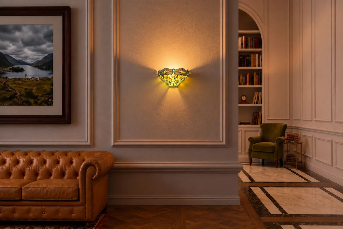 Tiffany wandlamp met kleurrijk libellendesign, sfeervol geplaatst op een lichte paneelmuur in een klassieke woonkamer met leren Chesterfield-bank en leeshoek | RORUVERA