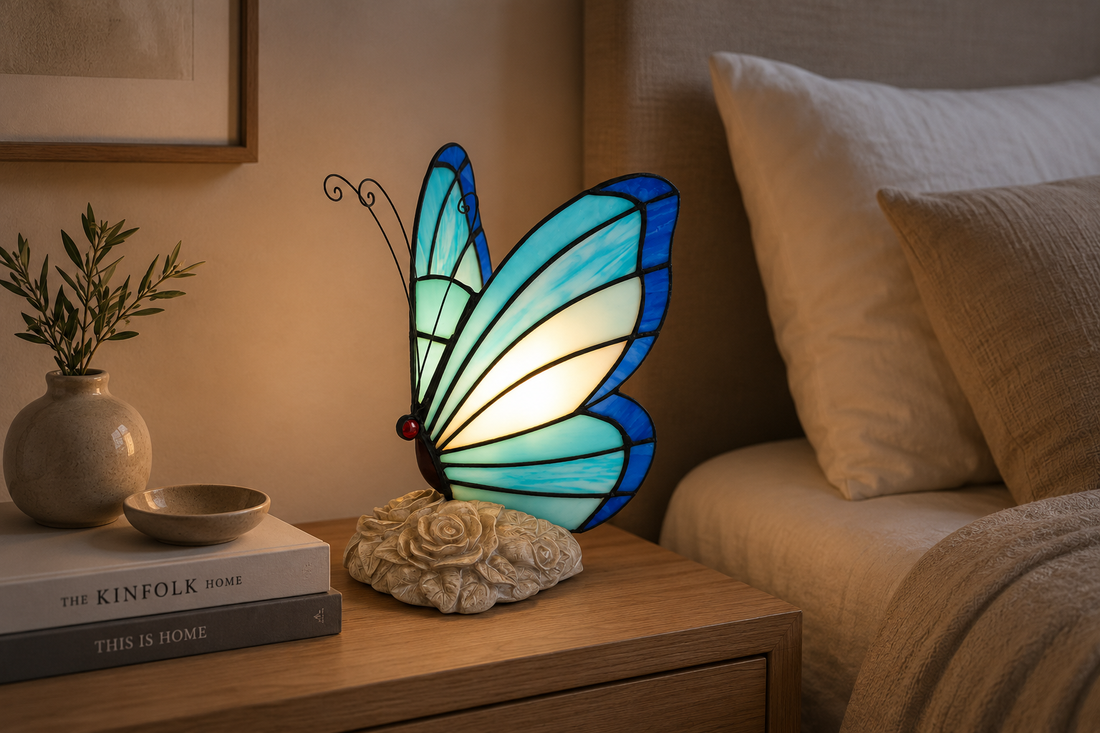 8000 - Blauwe Tiffany vlinderlamp met lichte rozenvoet op een houten nachtkastje naast een neutraal opgemaakt bed.